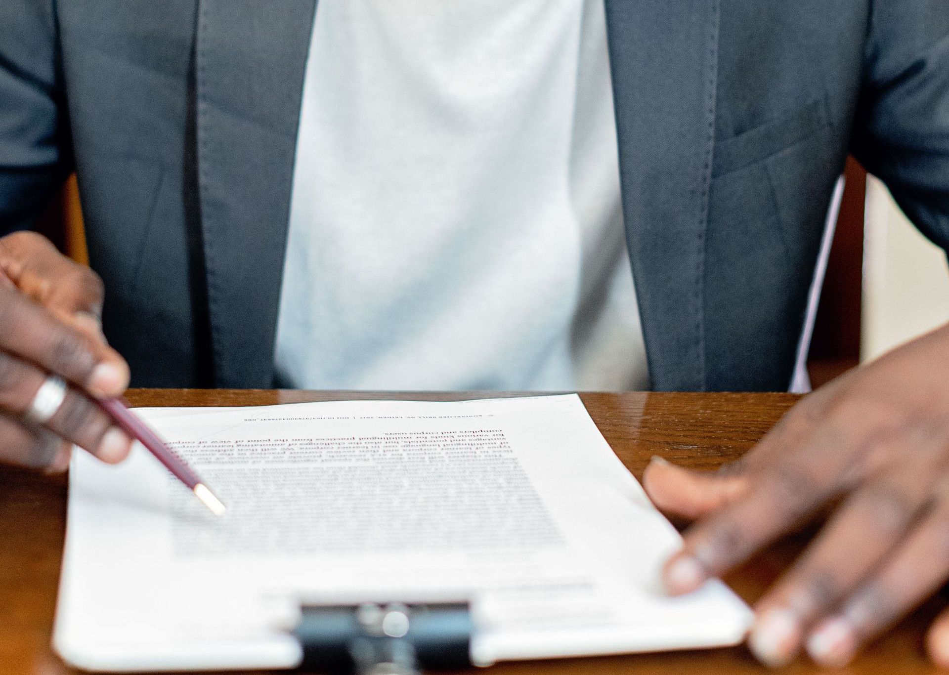 A focused businessman in a gray suit closely reviewing legal paperwork at a desk indoors.